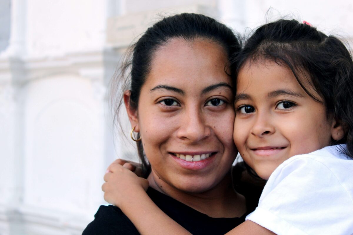 A woman holds a young girl in her arms and both are looking at the camera and smiling