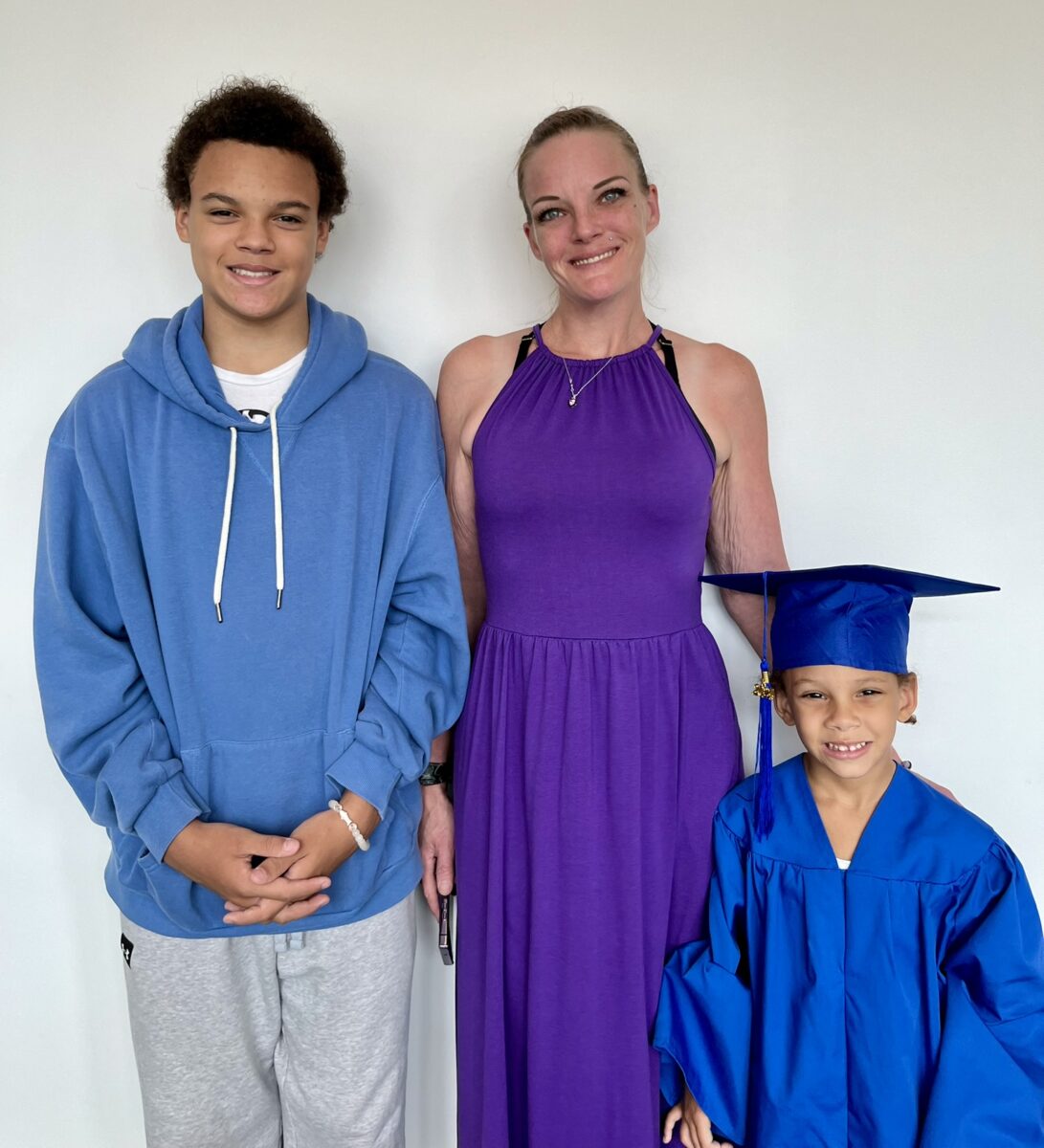 A woman with her teen son and her daughter in a cap and gown after preschool graduation