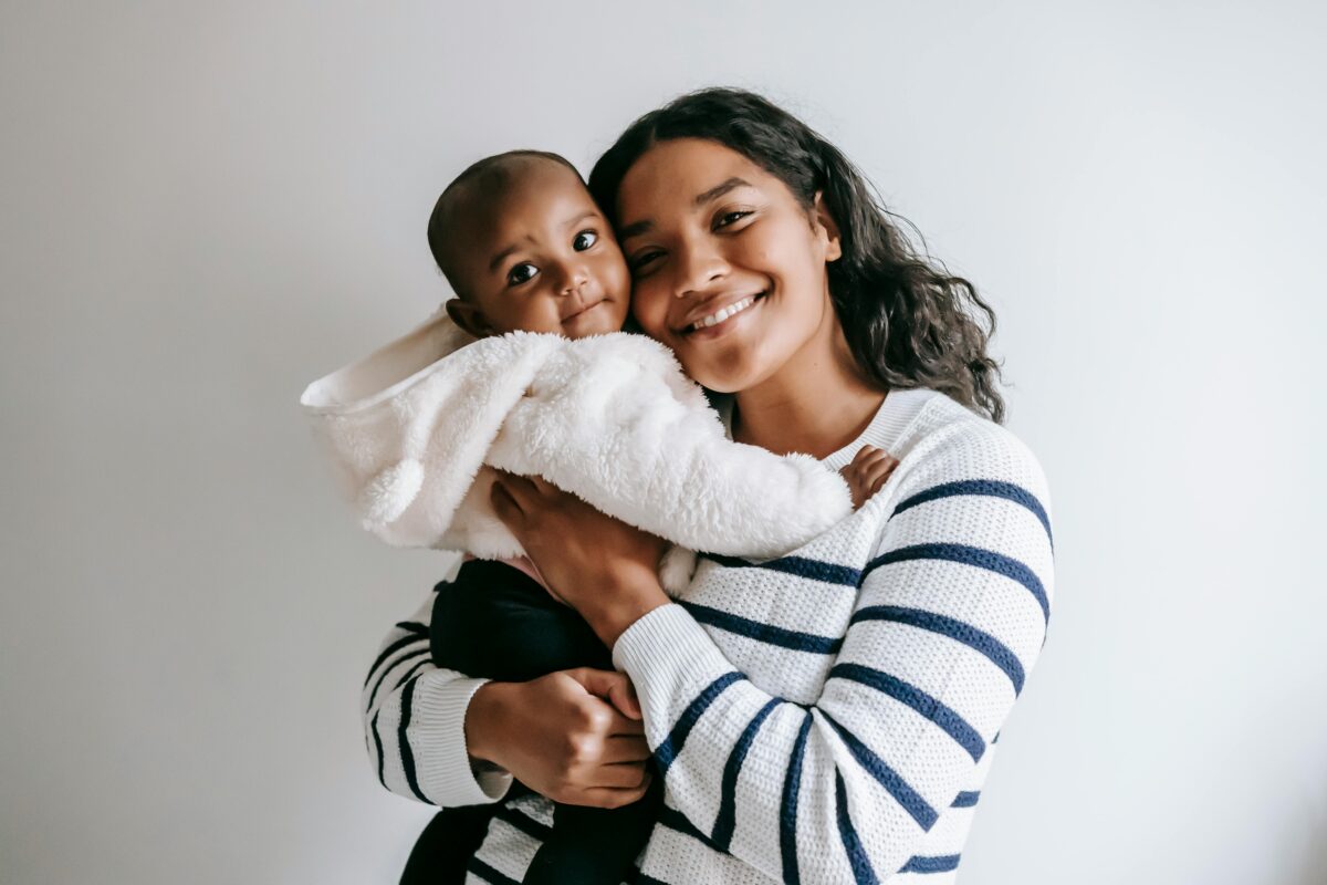 A young mother smiles warmly while holding her youngest child, reflecting the strength, love, and support families find through The Family Partnership's 2Gen programs.